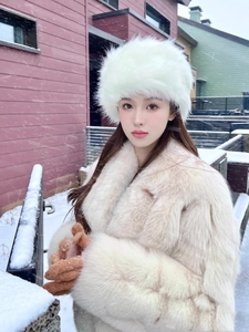 Detail of white faux fox fur hat with plush texture shown in a snowy outdoor setting