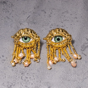 Detail of gold evil eye earring with green pupil and pearl tassel drops on grey surface