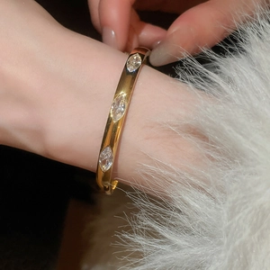 Macro detail of a gold bangle set with sparkling marquise-cut stones on white fur