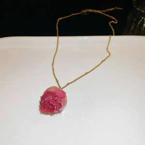Detail of dried pink rose pendant necklace with elegant gold bead chain and resin finish