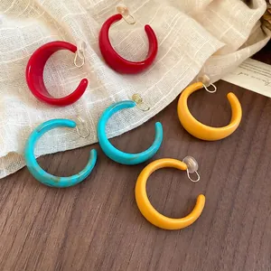 Three pairs of acrylic C-shaped clip earrings in red, turquoise marble, and yellow colors