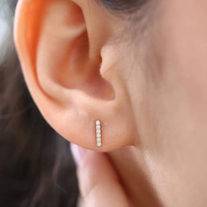 Macro shot of minimalist gold bar stud earring with five diamonds worn by a model