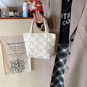 Detail of cream quilted handbag with rabbit embroidery pattern held by a person