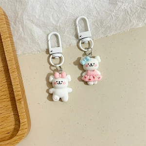 Dettaglio di due portachiavi a forma di orsetto bianco con fiocchi rosa e blu su beige