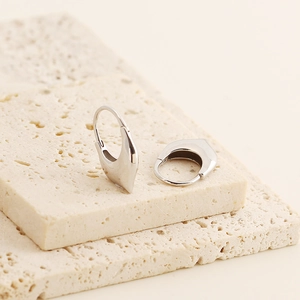 Macro detail of silver S925 U-shaped hoop earrings on minimalist stone surface