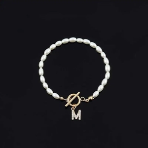 Elegant white oval pearl bracelet featuring a gold OT clasp and a sparkling letter M pendant