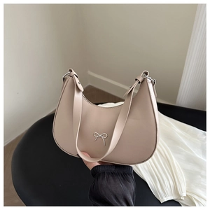 Detail of beige leather bag with small metal bow accent and wide shoulder strap