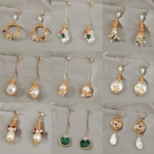 Boucles d'oreilles baroques dorées avec perles blanches et pierres sur fond de satin gris