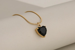 Detail of a gold snake chain necklace featuring a faceted black heart crystal pendant