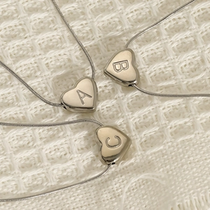 Polished stainless steel heart initial necklaces with delicate snake chains on white fabric