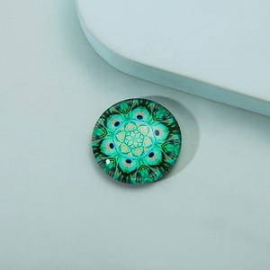 Detail of round crystal glass fridge magnet with green and blue peacock mandala pattern