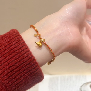 Vue rapprochée du bracelet doré 24K avec cordon de soie rouge et zircon scintillant