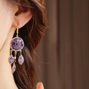 Detail of vintage gold earrings with purple zircon rhombs and tassels on model