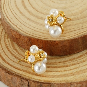 Macro shot of pearl flower stud earrings with gold petal accents on wooden background