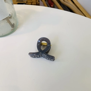 Close-up of dark grey minimalist hair claw clip with golden metal spring on white desk