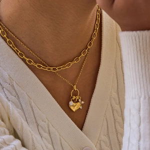 Detail einer mehrlagigen Goldkette mit Herzanhänger, weißer Perle und Sternanhänger
