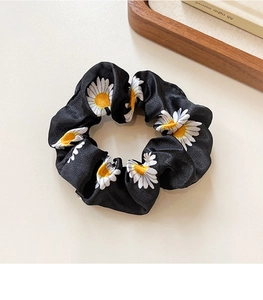 Detail of a black satin scrunchie with white daisy print and yellow center on a table