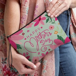Floral Mother's Day makeup bag in light green with zipper and hand strap held by model