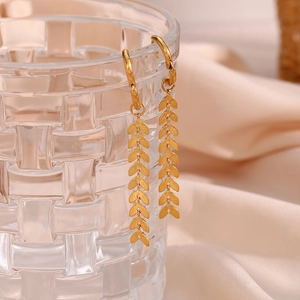 Detail of 18K gold-plated leaf drop earrings hanging on textured glass with silk background