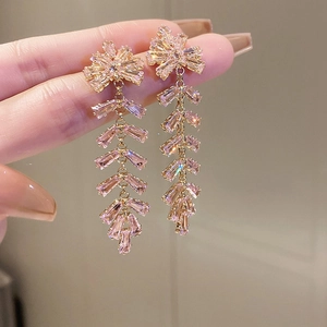 Detailed view of pink zircon drop earrings with gold metallic tassels held by hand