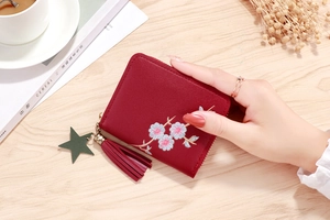 Detail of burgundy zip wallet with pink flower embroidery and a green star pendant