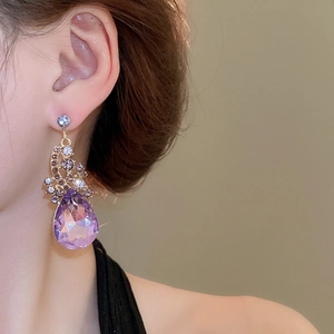 Detailed view of vintage-style earrings with large purple teardrop crystal on a model