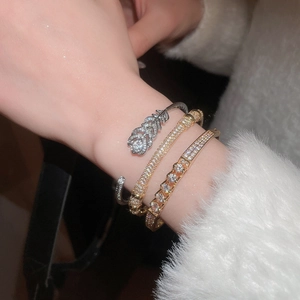 Close-up of stacked gold and silver bracelets with feather design and cubic zirconia