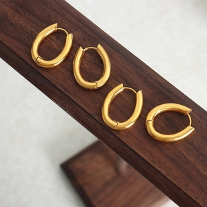 Two pairs of vintage oval gold titanium steel hoop earrings on a wooden display stand