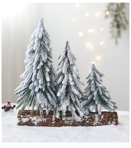 Three mini snow-flocked pine trees on wood base with festive bokeh background