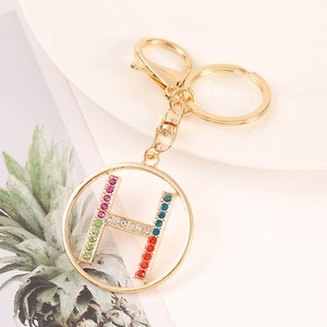 Close-up of golden letter H keychain with colorful rhinestones on white plate