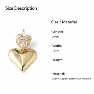 Detalle de pendientes de doble corazón bañados en oro con circonitas y 2,9 cm de longitud