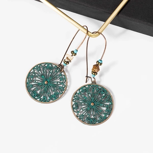 Close-up of vintage bohemian bronze hollow earrings with green patina and beadwork