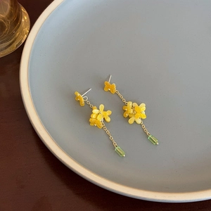 Detail of yellow flower tassel earrings with green crystal pendant on ceramic plate