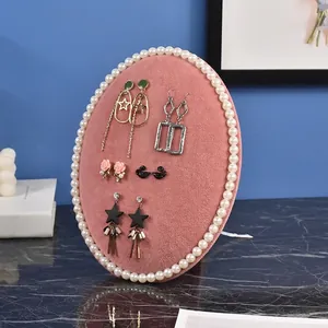 Pink velvet oval jewelry display tray with pearl trim showcasing assorted earrings