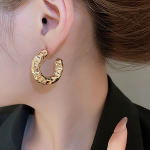 Detail of gold C-shaped hoop earrings with hammered texture worn by a model