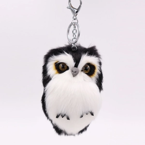 Close-up of a fluffy black and white plush owl keychain with large brown eyes and a metal hook