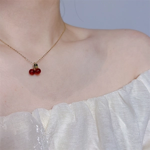 Detail of red cherry pendant necklace worn by model on a delicate gold chain