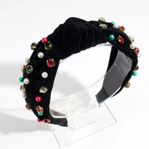 Close-up of black velvet knotted headband with colorful rhinestones and pearls on acrylic stand