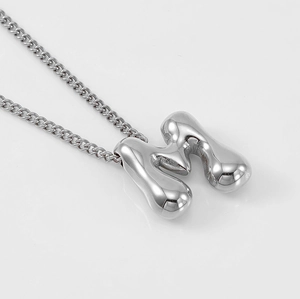 Macro shot of silver letter M pendant with liquid metal texture and mirror finish