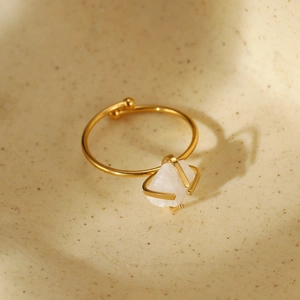 Adjustable gold stainless steel ring with white natural stone on a beige ceramic base