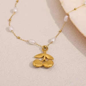 Detail of 18K gold plated necklace with cherry pendant and small pearls on beige background