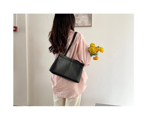 Minimalist black leather tote bag worn on shoulder by model in a clean lifestyle setting