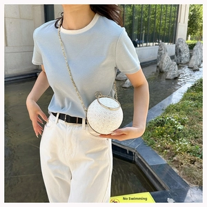 Outdoor view of an elegant round lace evening bag with golden ring handle and chain