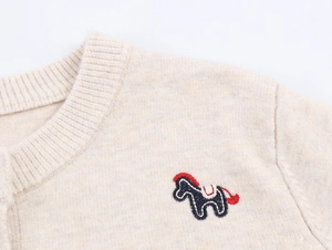 Close-up of cream knit cardigan featuring a detailed navy pony embroidery and ribbed collar