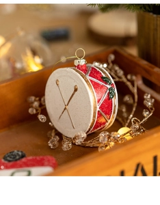 Detail of red and gold Christmas drum ornament with holly leaves on wooden tray