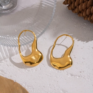 Detailed view of gold irregular fluid earrings on a minimalist textured surface with nature props