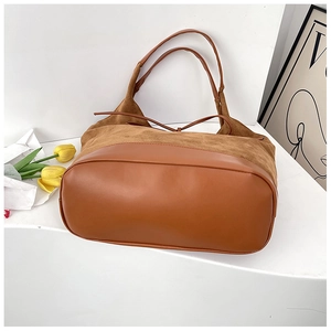 Detailed view of brown suede and leather patchwork tote bag on a minimalist background