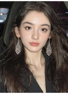 Detail of silver drop earrings with hollow filigree flower design worn on model's ear