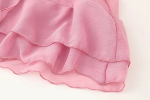 Détail de la jupe en mousseline rose avec ourlet festonné et volants superposés fluides