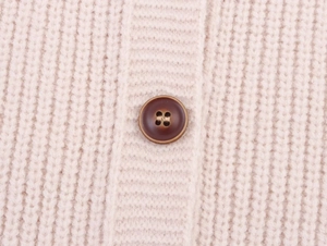 Detailed close-up of a brown button on a light beige chunky knit sweater cardigan